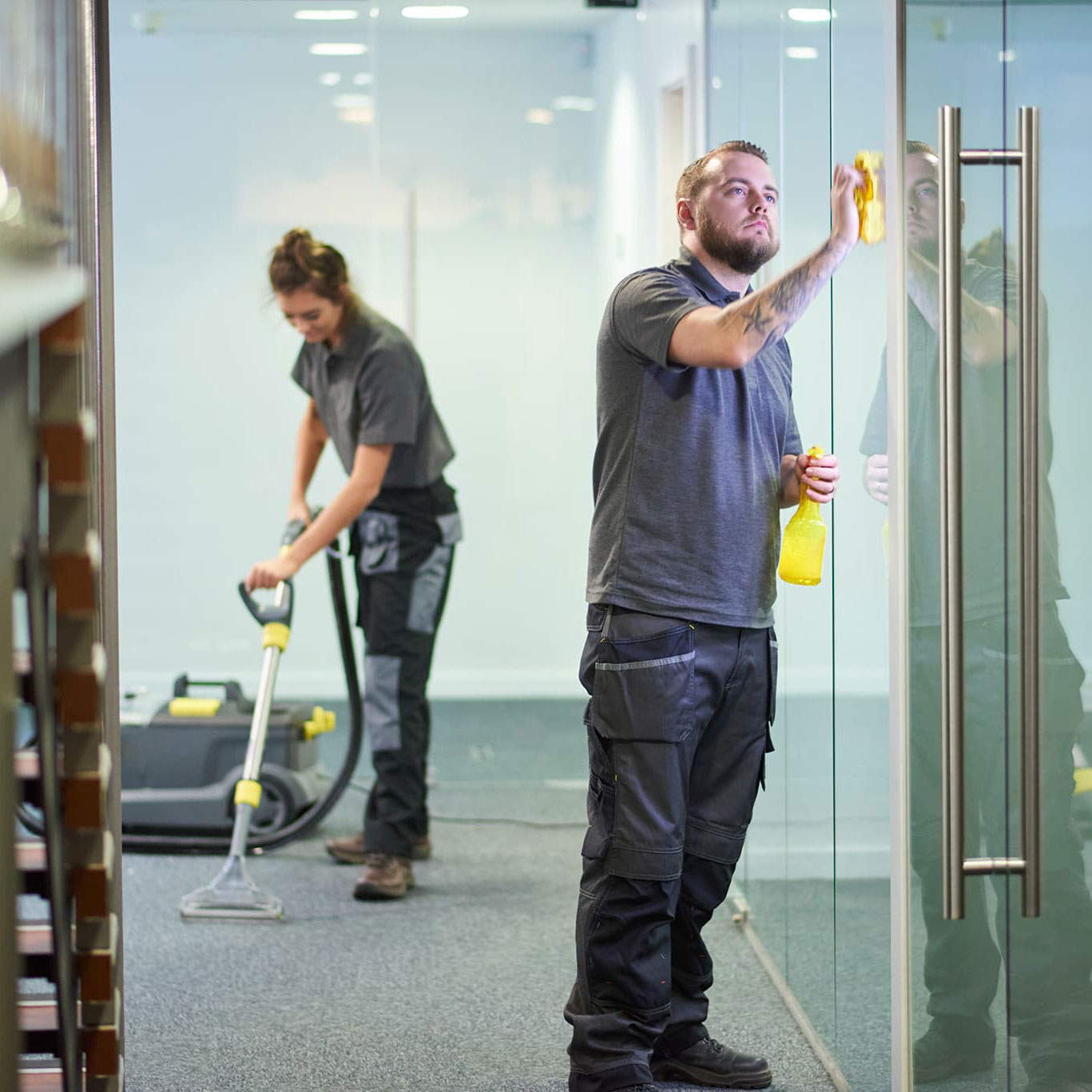 Zwei Fachkräfte vom Hausmeisterservice reinigen Glasflächen und Böden in einem modernen Bürogebäude für die besenreine Übergabe nach einem Mieterwechsel.