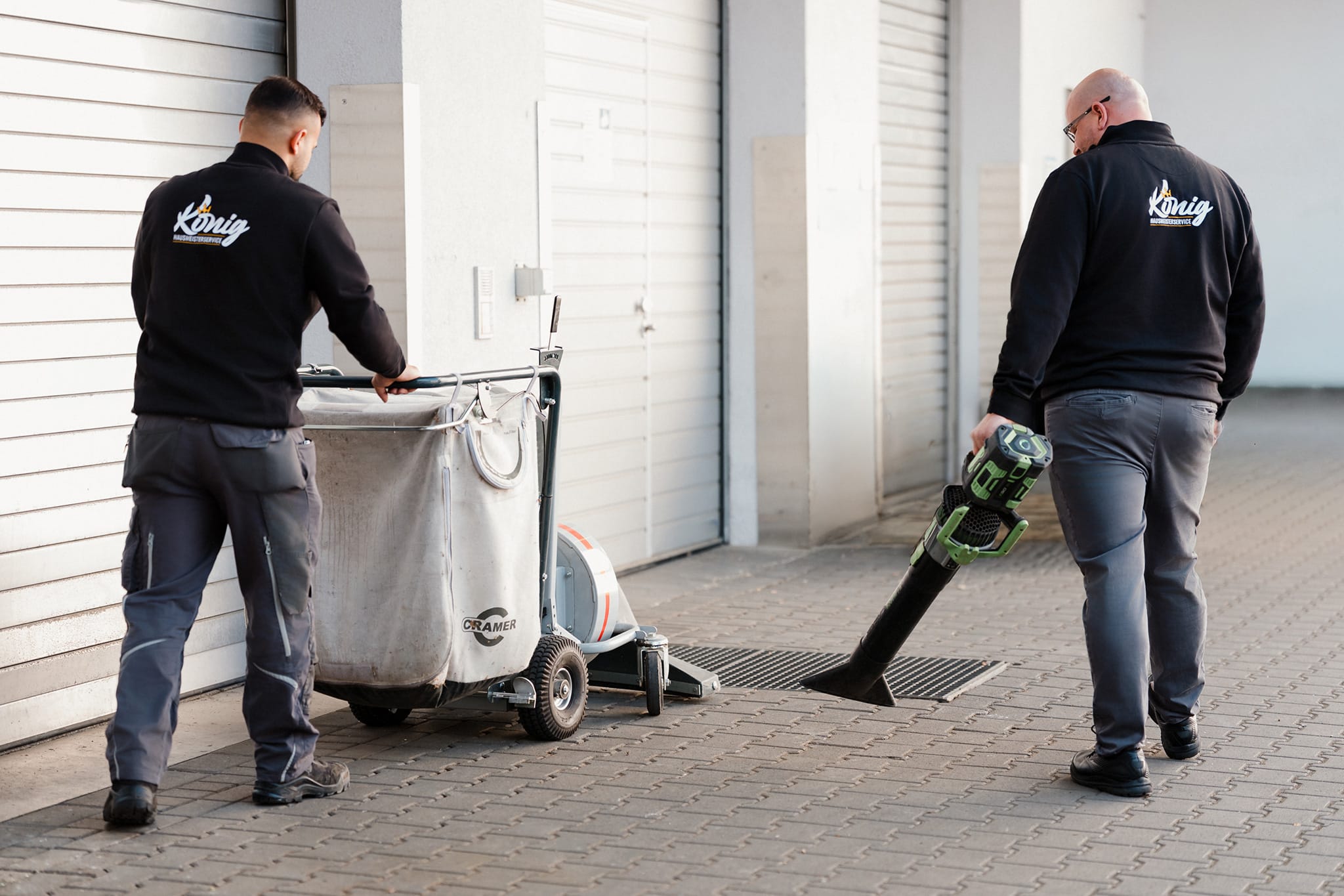 Zwei Mitarbeiter von König Hausmeisterservice bei der professionellen Wegereinigung und Laubentfernung auf einer gepflasterten Zufahrt, um saubere und sichere Außenbereiche zu gewährleisten.